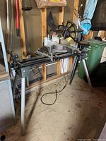 Full view of Hitachi digital and laser miter saw mounted on metal stand with 4 legs in garage setting