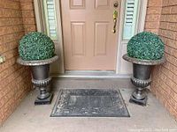 Both urn planters with faux boxwood bushes positioned on either side of front door.