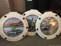 Three round white porthole style frames arranged side by side showing the three different lighthouse prints.
