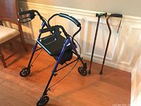 Blue Hugo rollator with padded seat, backrest, and ergonomic handlebars next to two walking canes, one brown and one patterned.