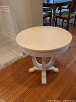 Front and top view showing round tabletop and curved four-legged base, painted white.