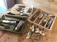 Tray and bins filled with mixed silverplate and stainless flatware and serving pieces, visible ornate handles and various cutlery types.