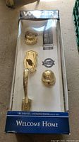 Complete Weiser door handle and deadbolt set in retail packaging with brass finish, visible handle style and included lock components.