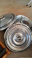 Group photo of all five hubcaps showing the design and condition including the dent on one Dodge hubcap
