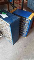 Two blue metal organizers with multiple transparent plastic drawers containing various hardware items, positioned on a concrete floor.