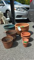 View of all plant pots including large green glazed planter, terracotta pots, and copper pots against a car background on pavement.