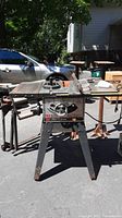 Full view of Sears Craftsman 10 inch table saw on metal stand outdoors in daylight. Shows tabletop, blade guard and legs.