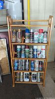Full front view of the wooden shelving unit with four shelves displaying assorted spray paints and two paint thinner bottles.