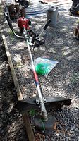 Full view of entire trimmer assembly laid on gravel with harness and cord bag beside