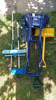 Photo showing all items in lot: two snow shovels (navy blue large and yellow small), three blue bristle brushes with handles (two extendable), and one long wooden handle.