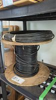 Photo of wood spool holding black wire coil with additional coil of wire on top, displayed on metal shelving.