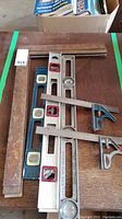 Overview of the squares and levels laid out on a wood surface showing two wooden framing squares, three spirit levels, and several metal squares