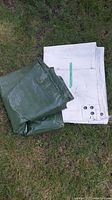 Two tarps folded and placed on grass; one green heavy duty tarp and one white heavy duty tarp.