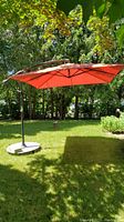 Full view of open red cantilevered umbrella with base stand in yard