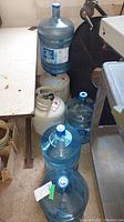 Four 18.9 L plastic water jugs and two white propane tanks placed on the floor.