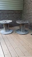 Photo showing two round wooden wire spools on a wooden deck against brick wall