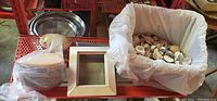 Photo showing round wooden boxes, small notebooks, a picture frame, and a large container of shells on a red metal shelf.