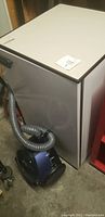 Indesit mini refrigerator top and Kenmore canister vacuum positioned on floor, showing condition and hose