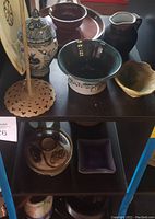 Top view of the pottery and ceramic items on black shelving including bowls, crock pot, candle stick holders, pitcher, and decorative plates.