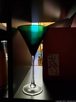 Green tinted wine glass with clear stem and base shown lit against dark background.
