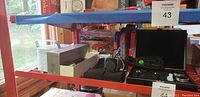 Shelf view showing assorted household gadgets including utensil sets, black carrying case, and other miscellaneous items