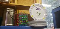 Photo showing metal household containers, drying rack with colorful outdoor wine glasses, and stacked floral plates