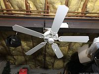 White ceiling fan mounted on ceiling showing 5 blades and metal supports.