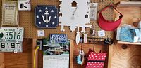 Photo of a mixed lot including a red sun visor hanging next to two wall clocks (one white cuckoo clock and one navy blue anchor-themed clock), a red polka dot lunch bag, vintage National Geographic magazine and two vintage license plates from New Hampshire and Connecticut.