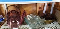 Photo showing Vintage Visions amber glass cookware set with several round pots and pans with transparent amber lids and four clear square Pyrex baking dishes stacked together.