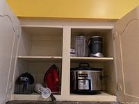 Kitchen appliances in cabinet: NutriBullet blender with container, CrockPot slow cooker, Cuisinart Smart Stick hand blender, KitchenAid hand mixer.