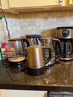 Five kitchen appliances: four electric kettles and one Black & Decker coffee maker arranged on countertop.