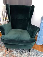 Front angled view showing green velvet upholstery, wingback design, padded arms and wooden legs
