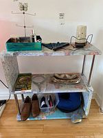 Overall lot displayed on multi-tiered shelf with world map print, showing jewelry stand, diffuser, fan, shoes, cushions and boxes with miscellaneous items.