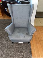 Front view of gray upholstered IKEA child's chair showing armrests, button details on backrest, and stains on upholstery.