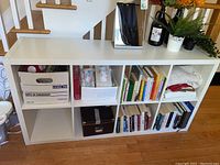 Wide view of white IKEA shelf placed horizontally, filled with boxes, books, tissues, and decorative items on top.
