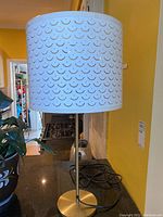 Full side view of metal table lamp with perforated pattern white metal shade and brushed metal stand on kitchen counter.