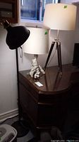 Three lamps in a room on and near a table; one floor lamp with black adjustable head and two table lamps with white drum shades and decorative bases.