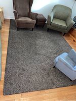 Photo showing the brown rug surrounded by different chairs on a wood floor.