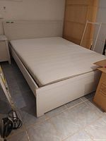Full view of the queen size bed with white padded headboard and mattress included. Bed frame is white with matching footboard.