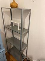 Metal shelving unit with four shelves, small white metal shelf on the second tier, and wooden essential oil diffuser on top