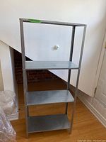 Front view of metal shelving unit with four shelves and scratches on shelves and frame.