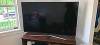 Front view of TV on wooden stand with window in background
