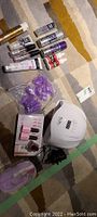 Photo of assorted nail polish bottles, nail care products, and LED nail curing lamp on carpet.
