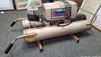 Side angle photo showing the full Campbell Hausfeld Super Pal air compressor with cylindrical tank and motor unit on top, along with handles and warning label.