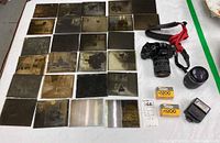 Full overview of 28 antique glass negatives laid out alongside the Ricoh KR-5 Super II camera with attached 35-70mm lens, Takumar 135mm lens, Takumar flash, and two rolls of Kodak P3200 film.