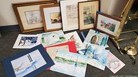 View of framed and unframed original art and prints including watercolor paintings, sketches, and lithograph laid on the floor and leaned against the wall