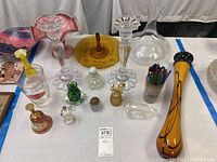 Full view of the lot showing various glassware including two tall clear glass candle sticks, decanter, pitchers and small decorative glass items arranged on a table.