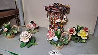 Porcelain floral figurines arranged with musical carousel in center showing flowers and candle holders