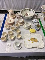 Full view of the tea set pieces arranged on a white tablecloth, including teacups, saucers, small bowls, a pitcher, trinket boxes, and a large decorative bowl with bird motifs.