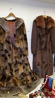 Two vintage women's long fur coats hanging side by side on a wall.